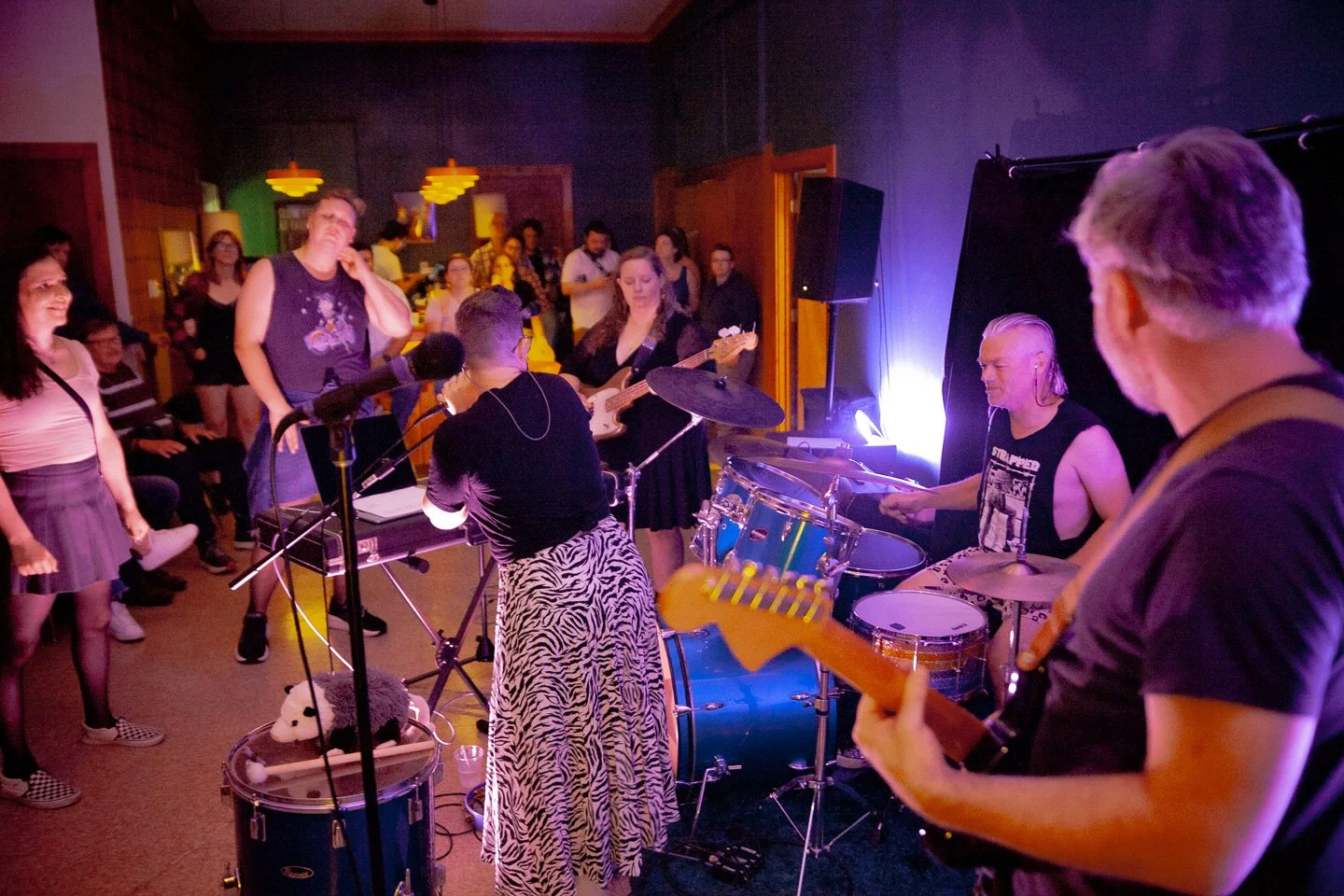 Live band performing on stage with audience watching at an indoor venue.