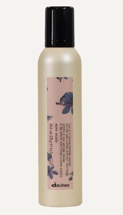 A beige spray bottle with a black cap, featuring a pink label with blue bees and text branding 'Davines'.
