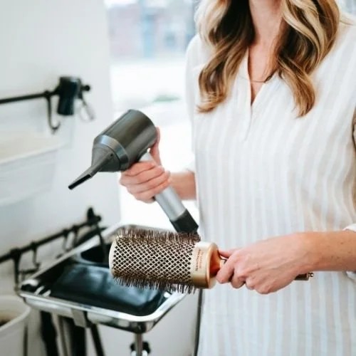 Hairstylist using a blow dryer on a round hairbrush in a salon.