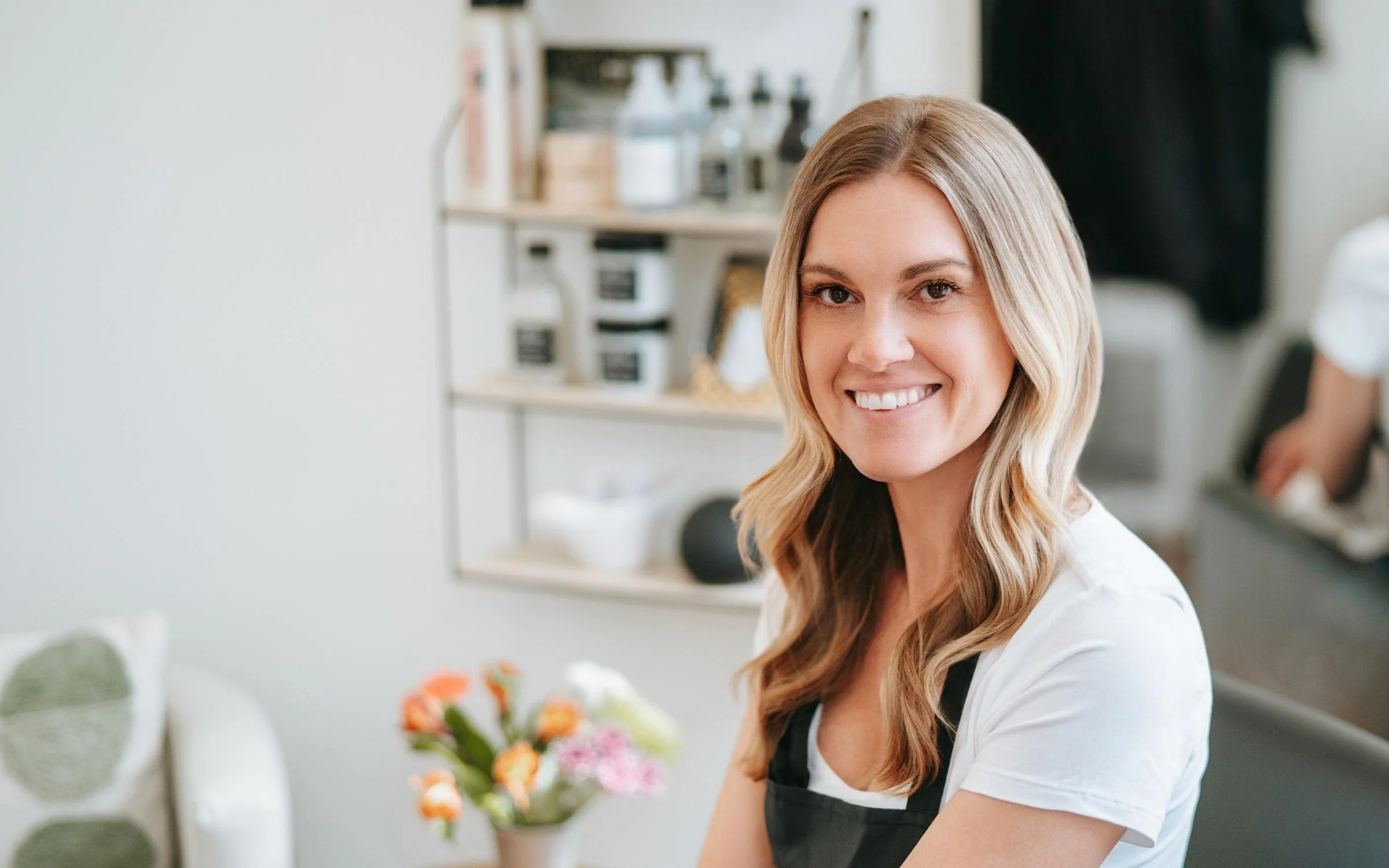 A woman with long, blond hair smiling while holding a bouquet of mixed flowers in a Colorado Springs hair salon.