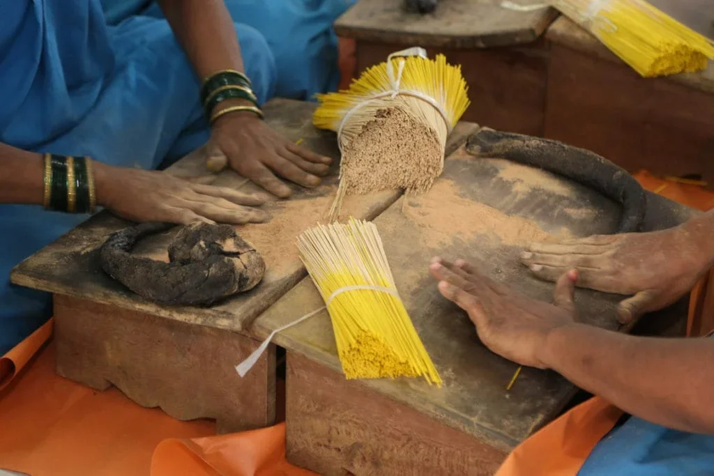 People pressing dough and drying pasta on a wooden table, with bundles of uncooked spaghetti nearby.