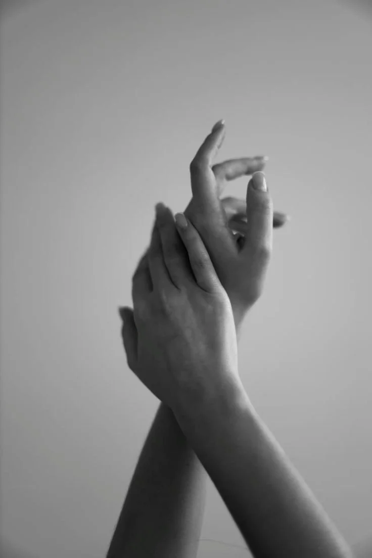Close-up of two hands gently intertwined in a black and white photo against a plain background.