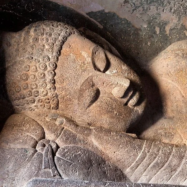Close-up of a carved reclining Buddha statue made of stone, showcasing detailed facial features and textured hair.