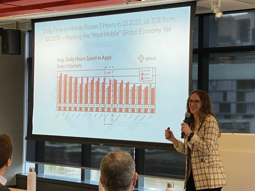 Our Chief Analyst giving a presentation in a conference room. She is holding a microphone and standing beside a large screen displaying a chart on mobile app usage and global economy.