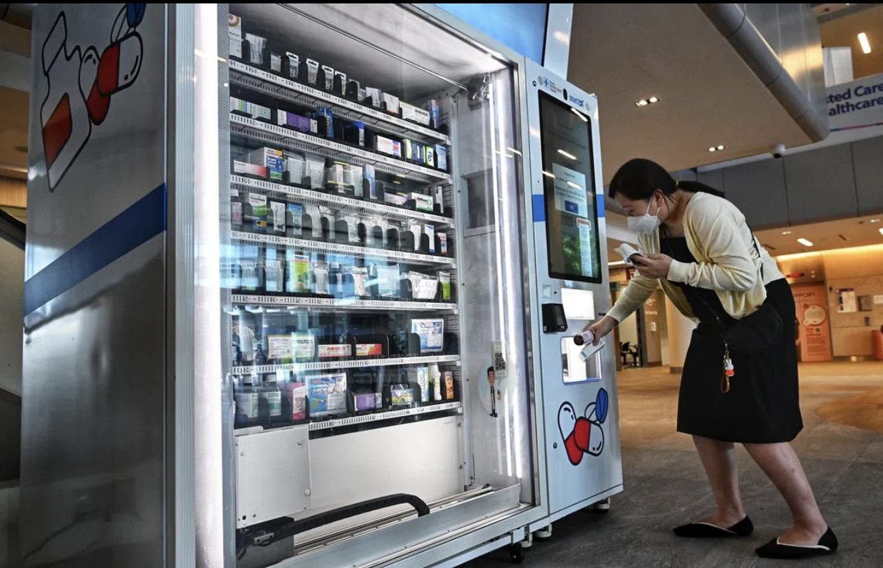 A woman in a face mask is buying medicine from a vending machine in a shopping mall.