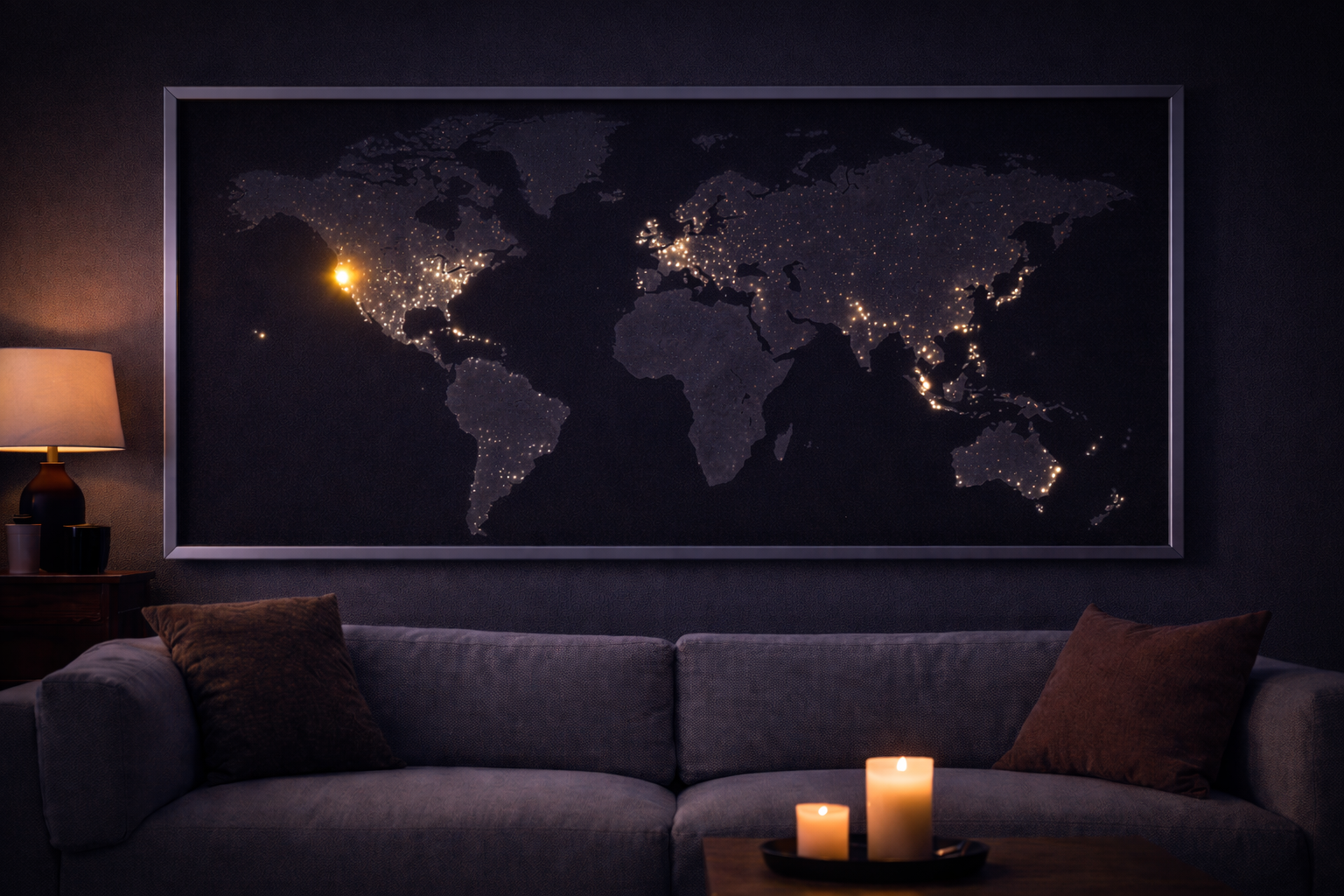 Dark living room with a large world map illuminated by city lights, a gray sofa with brown pillows, a side table with a lamp, and candles in the foreground.