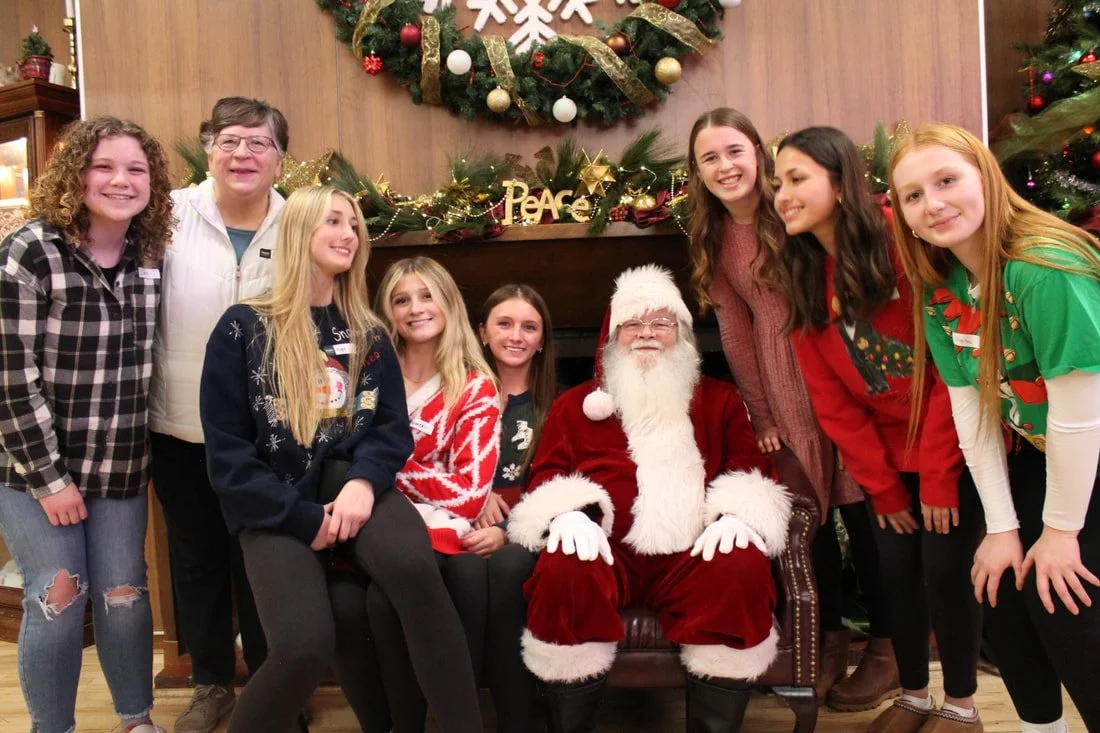 Children with Santa Claus at a Christmas event in front of a decorated fireplace and Christmas tree.