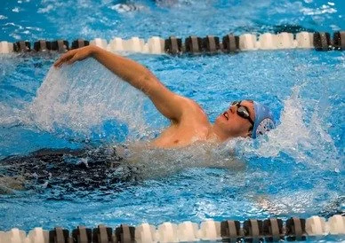 Swimmer in a swimming pool performing a freestyle stroke wearing goggles and a swim cap.