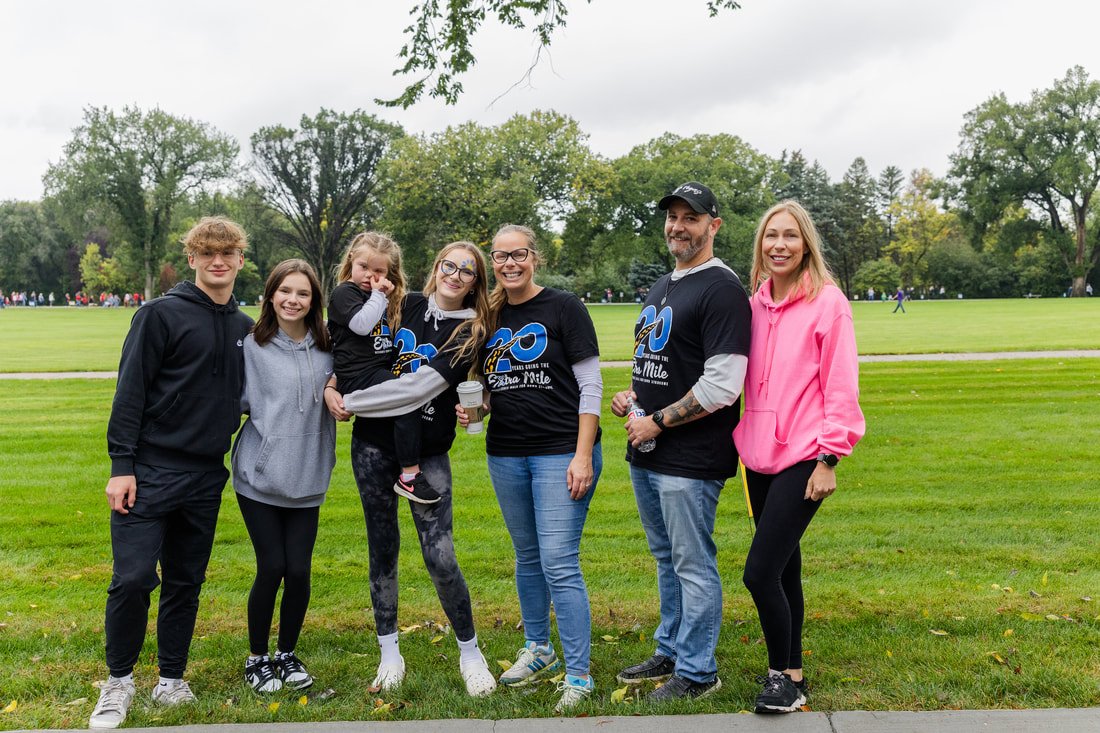 Group of six people, including children and adults, standing on a grassy field with trees in the background, smiling and posing for the photo.