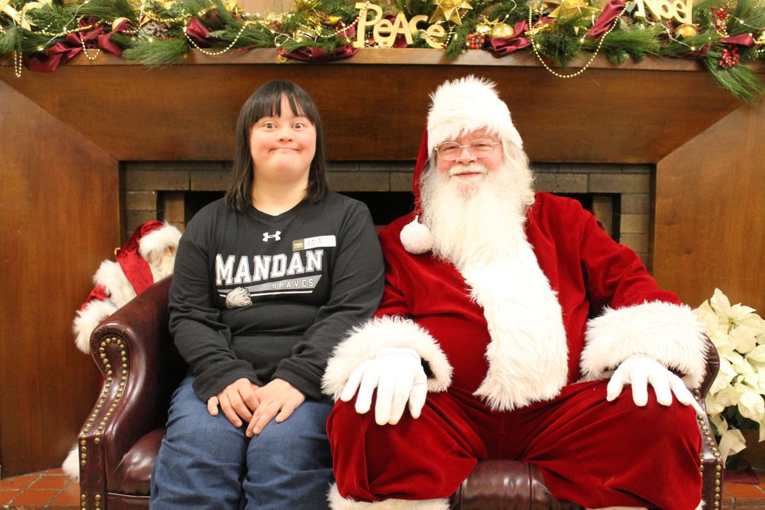 A girl sitting next to Santa Claus on a decorated Christmas fireplace mantel with holiday decorations.