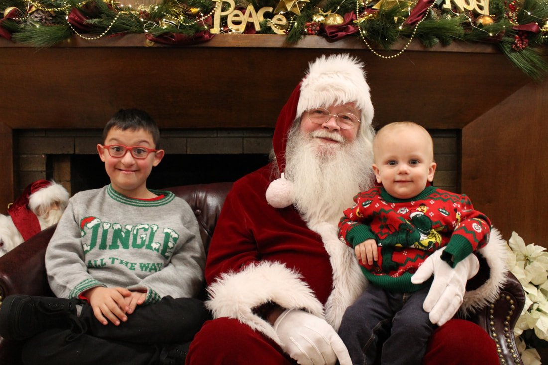 Two children sitting with Santa Claus in front of a decorated fireplace for Christmas.