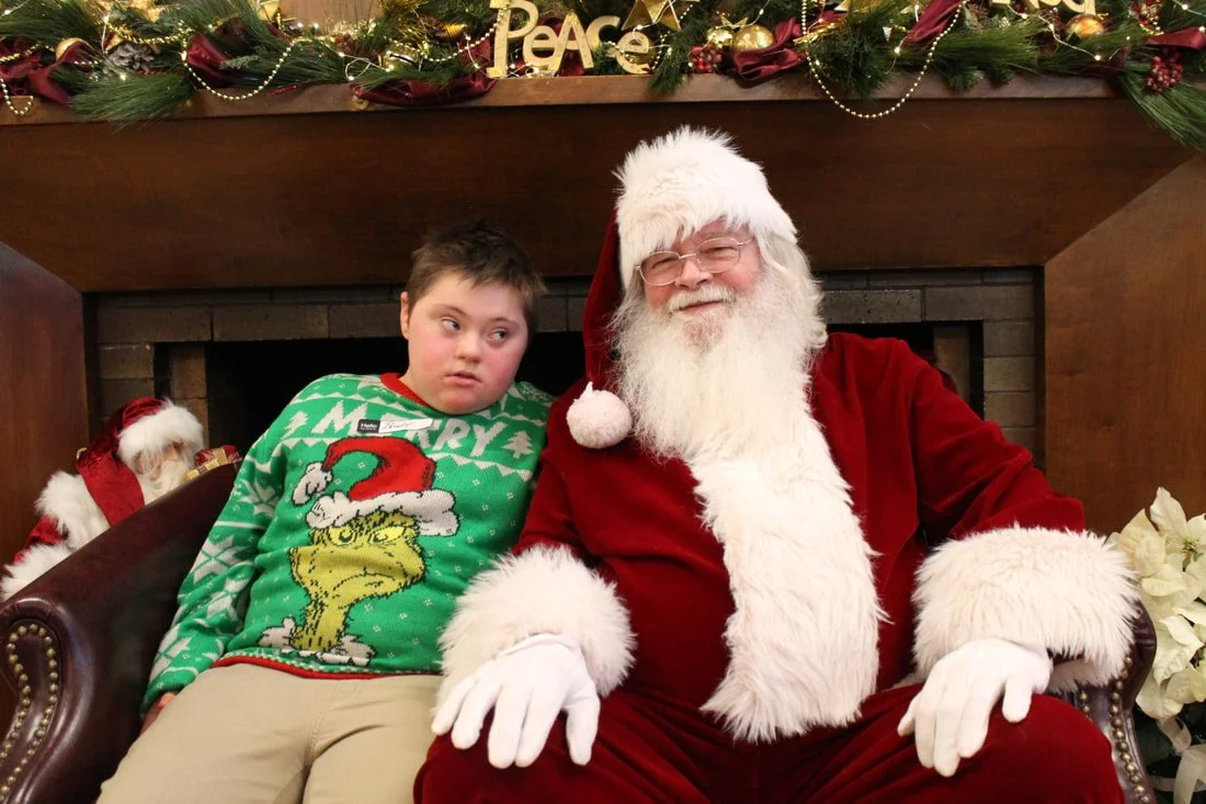 A boy sitting next to Santa Claus during a Christmas event, with holiday decorations including garland and 