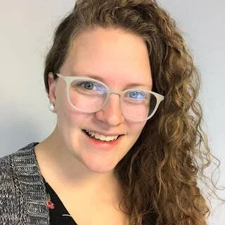 A woman with long curly hair, glasses, and earrings smiling at the camera.
