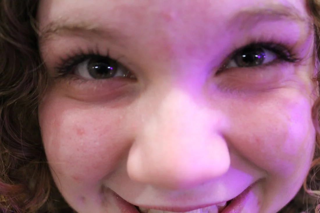 Close-up of a smiling young girl with curly hair, gray eyes, and visible freckles.