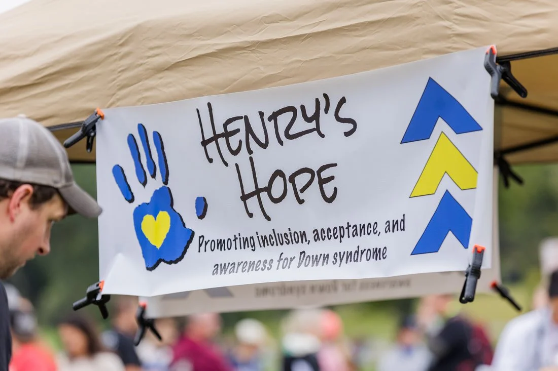 Banner for Hendry's Hope promoting inclusion, acceptance, and awareness for Down syndrome, featuring a blue and yellow handprint and blue and yellow arrows.