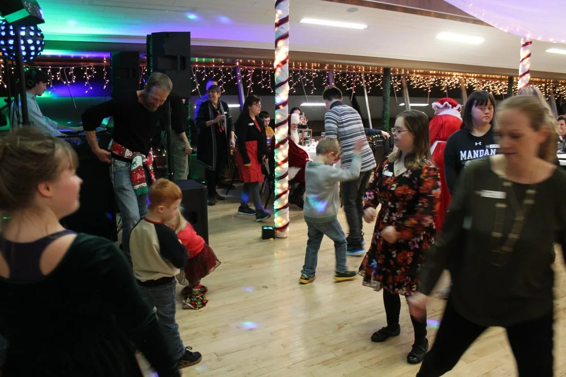 People dancing at a Christmas party with festive decorations, string lights, candy cane poles, and a DJ setup in the background.