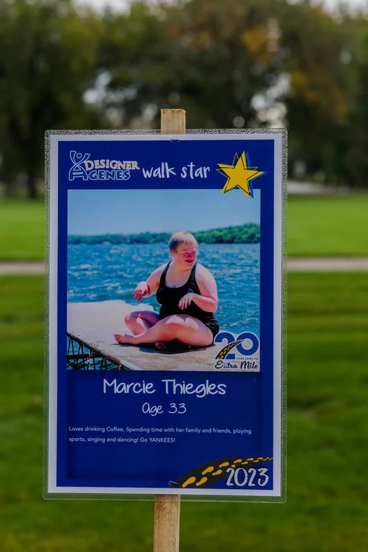 A sign with a photo of a woman sitting by a lake, water in the background, and text promoting an event or celebration in 2023.