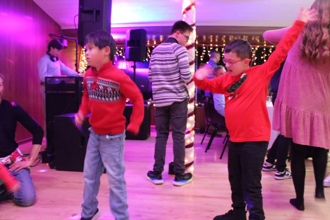Children dancing at a party with colorful lights and a DJ in the background.
