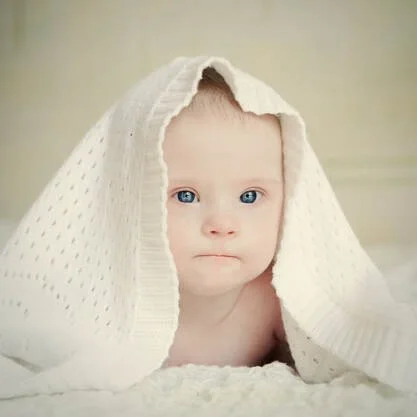 Baby with blue eyes covered by a white blanket.