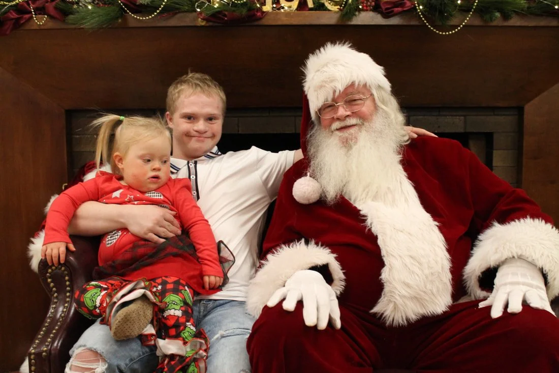 Children sitting with a man dressed as Santa Claus in front of a decorated fireplace mantel.