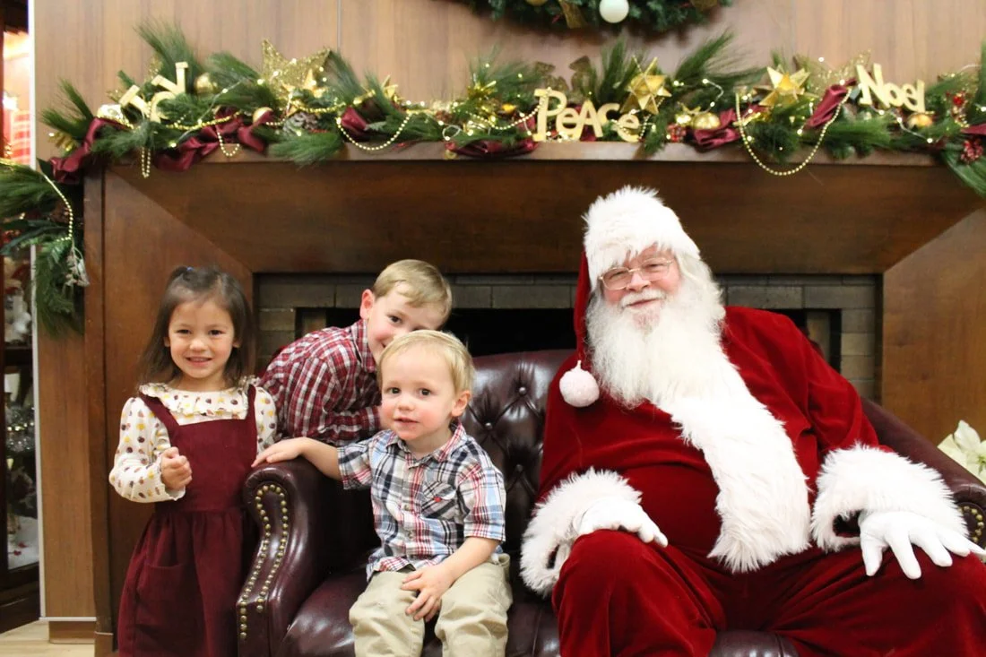 Three children and Santa Claus sitting in front of a decorated fireplace for Christmas