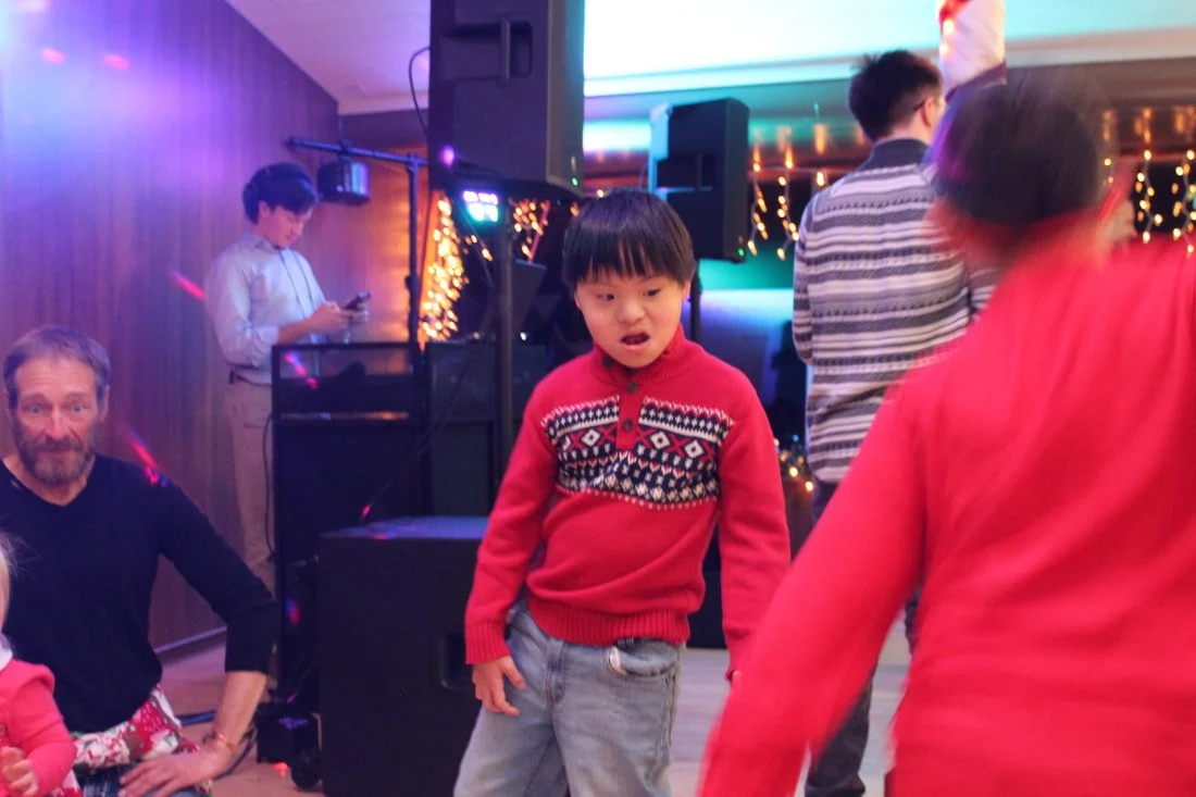 Children and adults dancing and socializing at a festive indoor party with colorful lights and decorations.