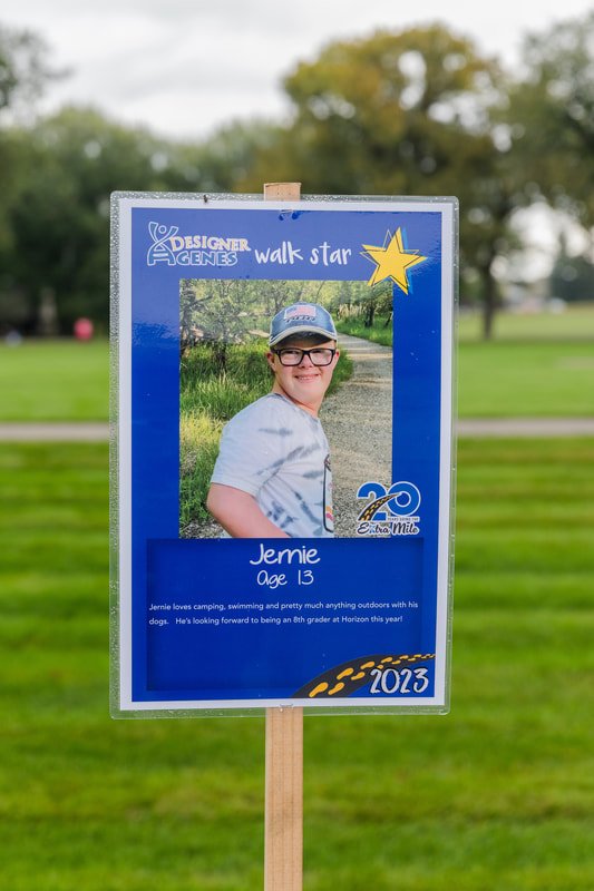 Sign with young girl’s photo, her name Jenie, age 13, and description of her hobbies and aspirations, set outdoors in a park, with trees and grass in the background.