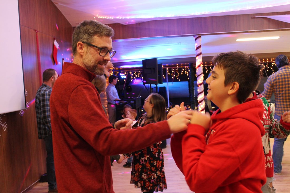 A man and a boy are dancing together at a holiday party, decorated with string lights and candy cane poles.