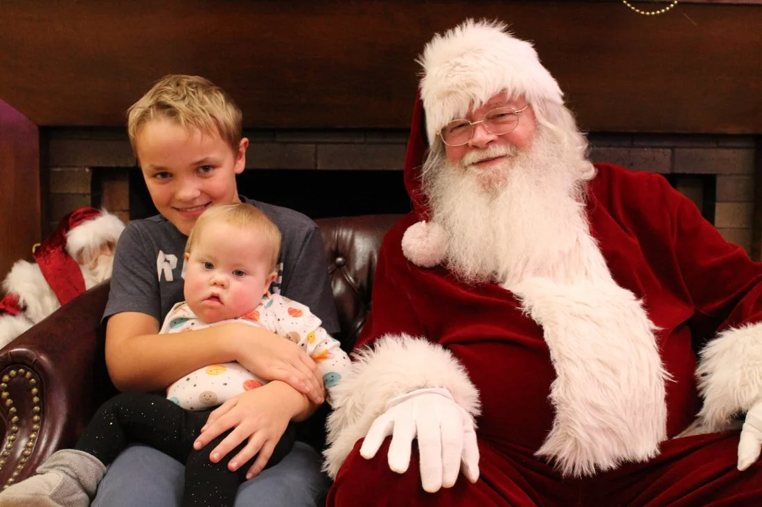 Two boys sitting with Santa Claus in a festive setting.