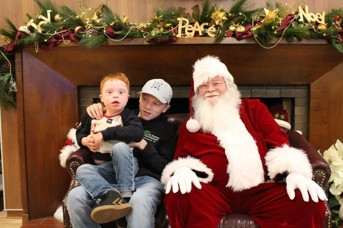 A young boy and a teenage boy sitting with Santa Claus in a Christmas setting with decorations and a fireplace