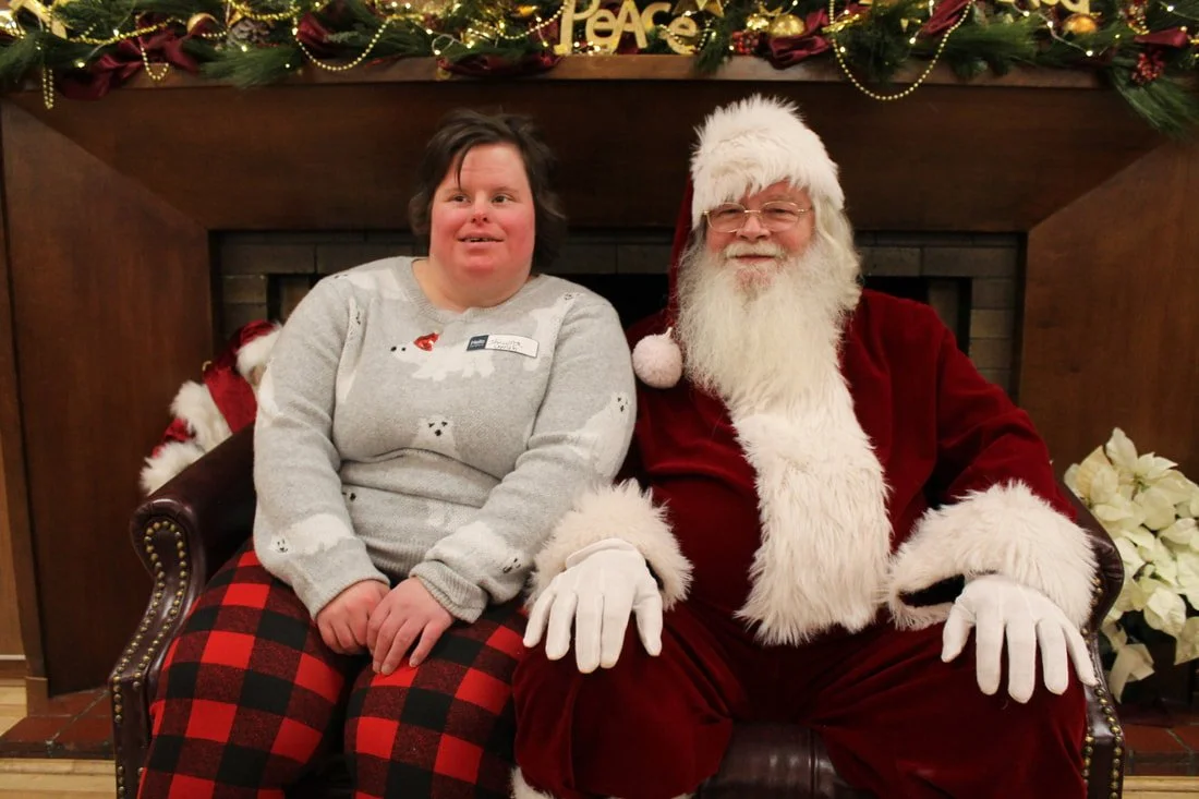 A woman sitting next to Santa Claus on a decorated Christmas mantle.