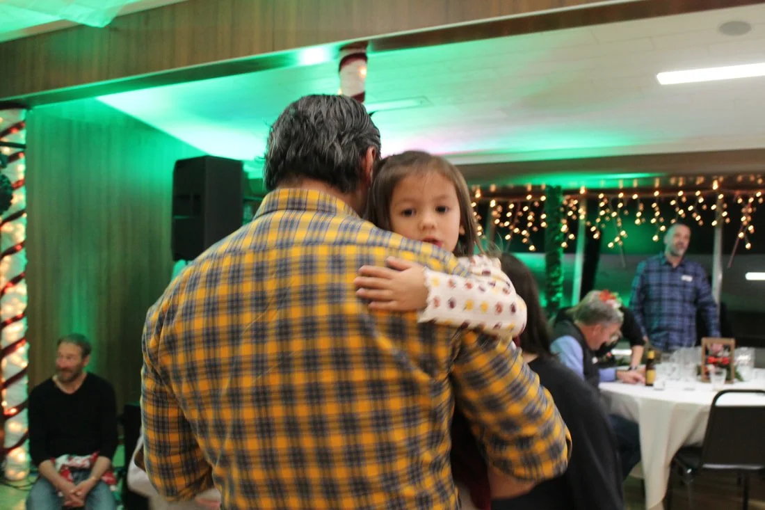 A man holding a young girl at a festive indoor gathering with Christmas lights and decorations.