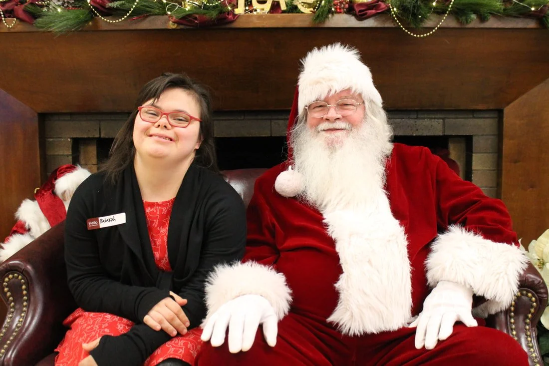 A girl sitting next to Santa Claus in a Christmas setting with holiday decorations.