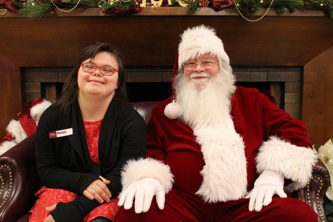 A young girl sitting on Santa Claus's lap, both smiling, in a festive setting with Christmas decorations.