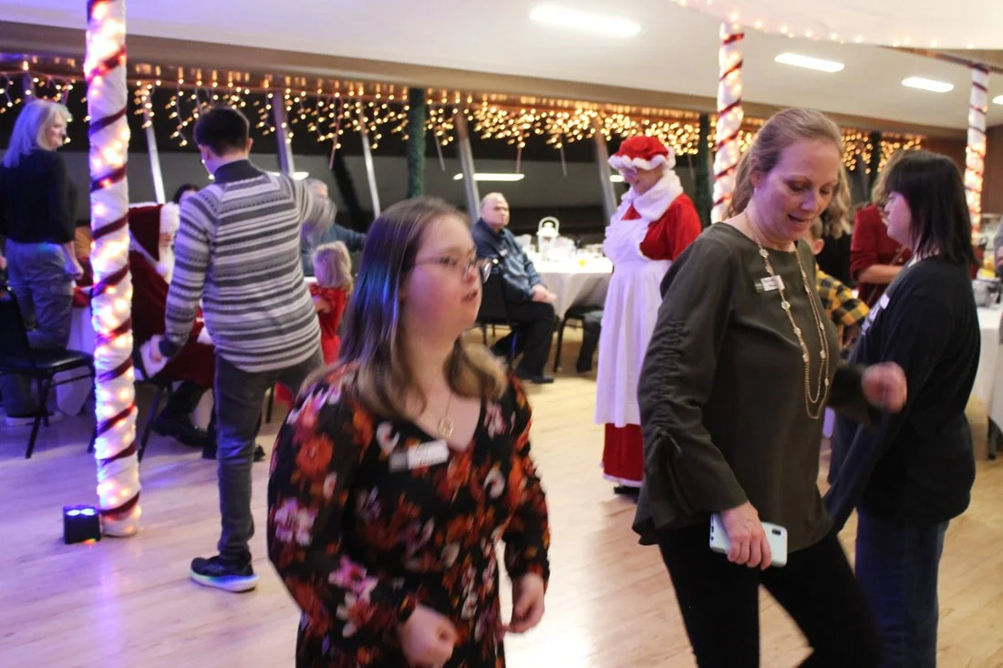 People gathered at a Christmas party with festive decorations, including candy cane columns and string lights, and a person dressed as Santa Claus.