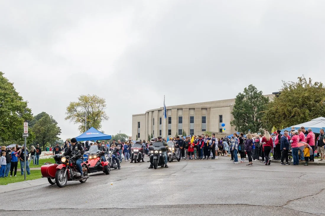 People gathered outside a government building, with motorcycles and a tent, during a community event.