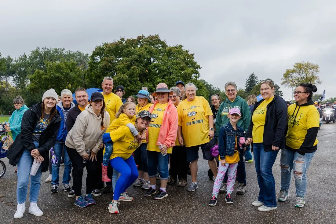 Group of people wearing yellow and black Minions-themed shirts, gathered outdoors for a fun event on a cloudy day.