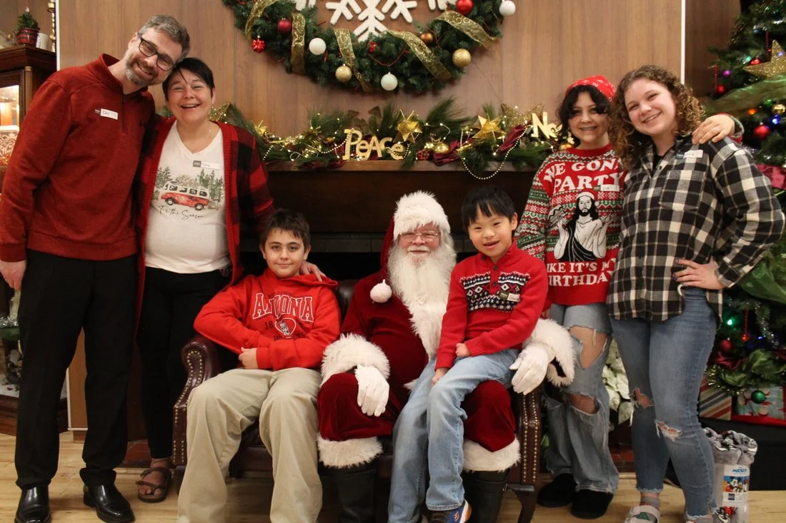 Family and Santa Claus posing in front of Christmas decorations with a wreath, ornaments, and stockings.