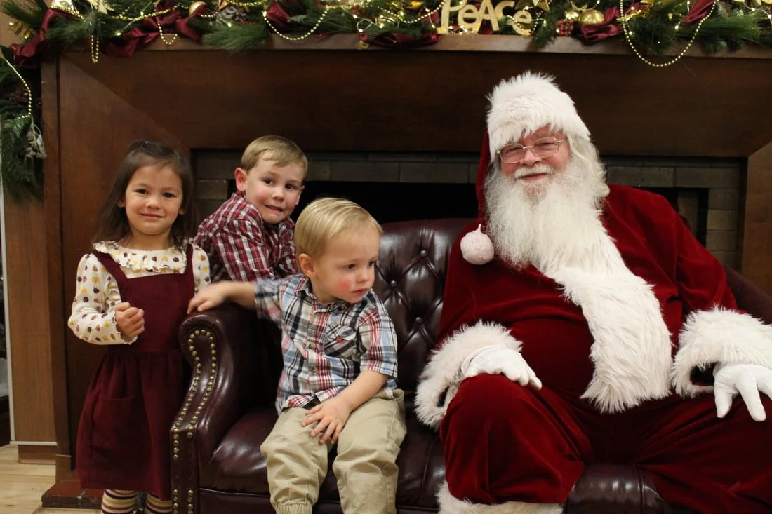 Children sitting with Santa Claus in front of a decorated fireplace mantel during Christmas.