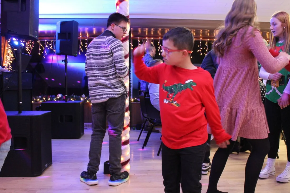 Children dancing and socializing at a holiday party with Christmas lights and decorations.