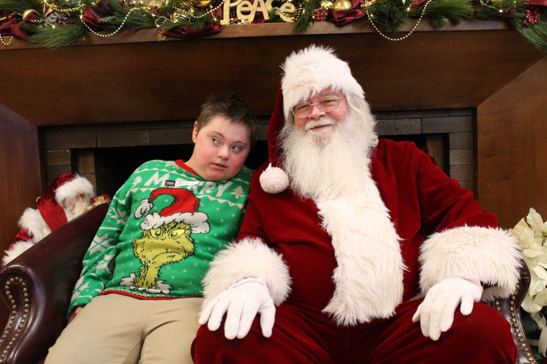 A boy sitting next to Santa Claus in front of a fireplace decorated for Christmas.