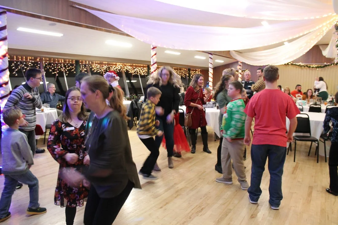 People dancing and socializing at a holiday party with Christmas decorations and string lights.