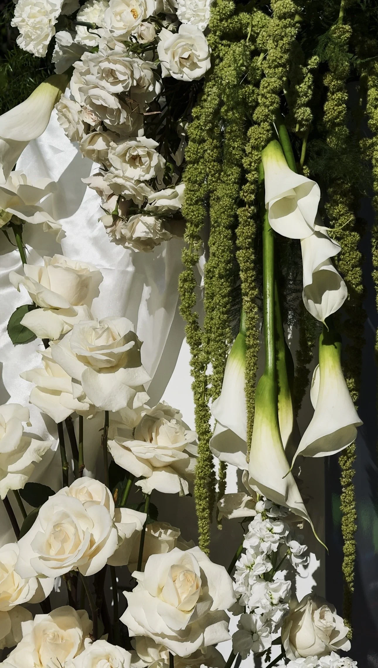 Arrangement of white flowers, including roses, calla lilies, and other blooms, with green foliage.