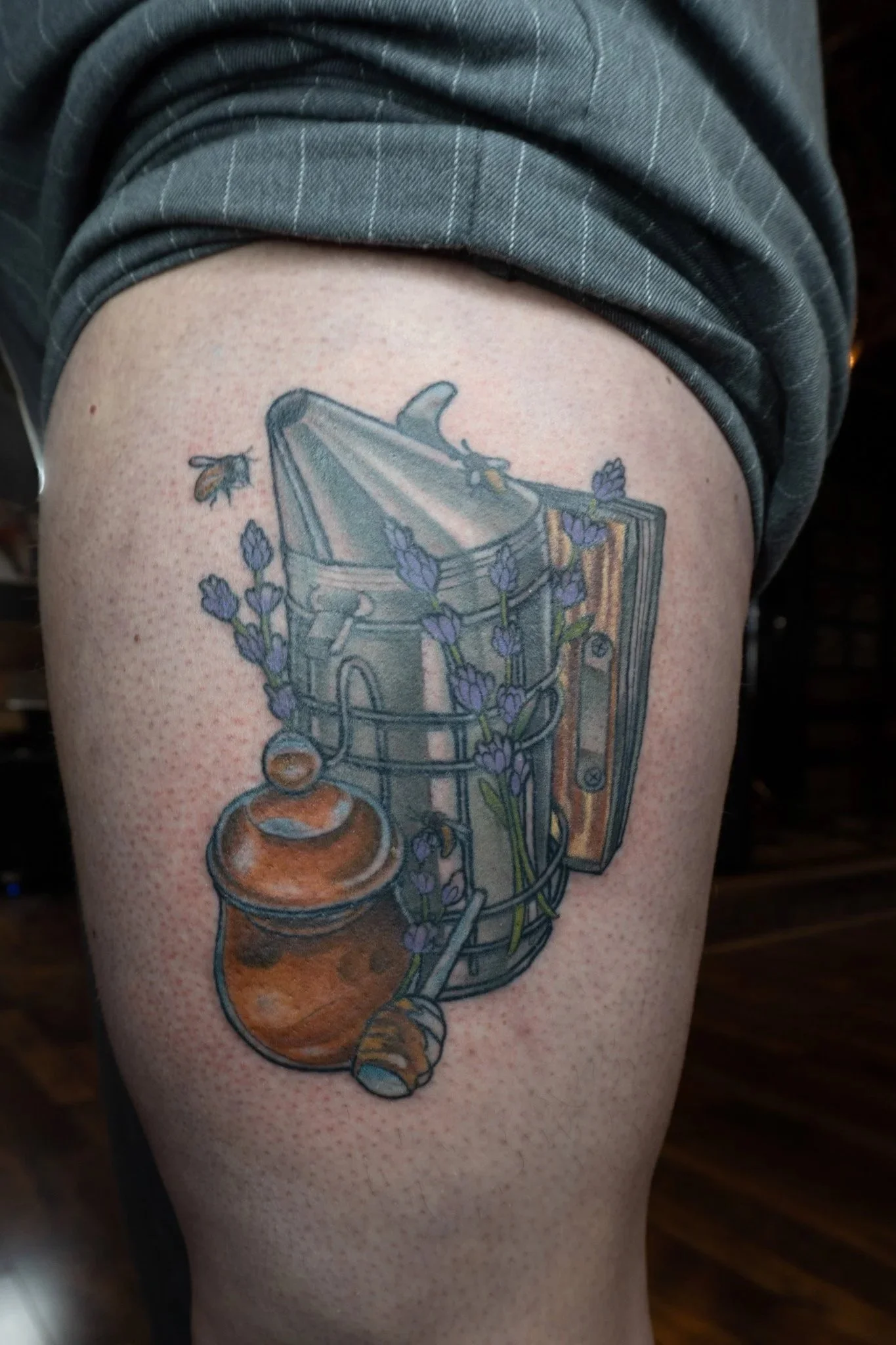 Tattoo of a lantern with lavender flowers and a honey jar with a bee on a person's thigh.