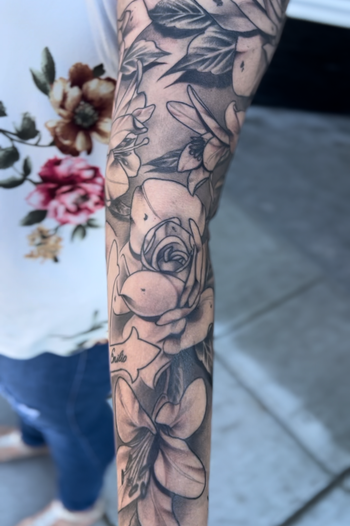 Close-up of a person's arm with a black and gray floral tattoo sleeve, including roses and a butterfly.