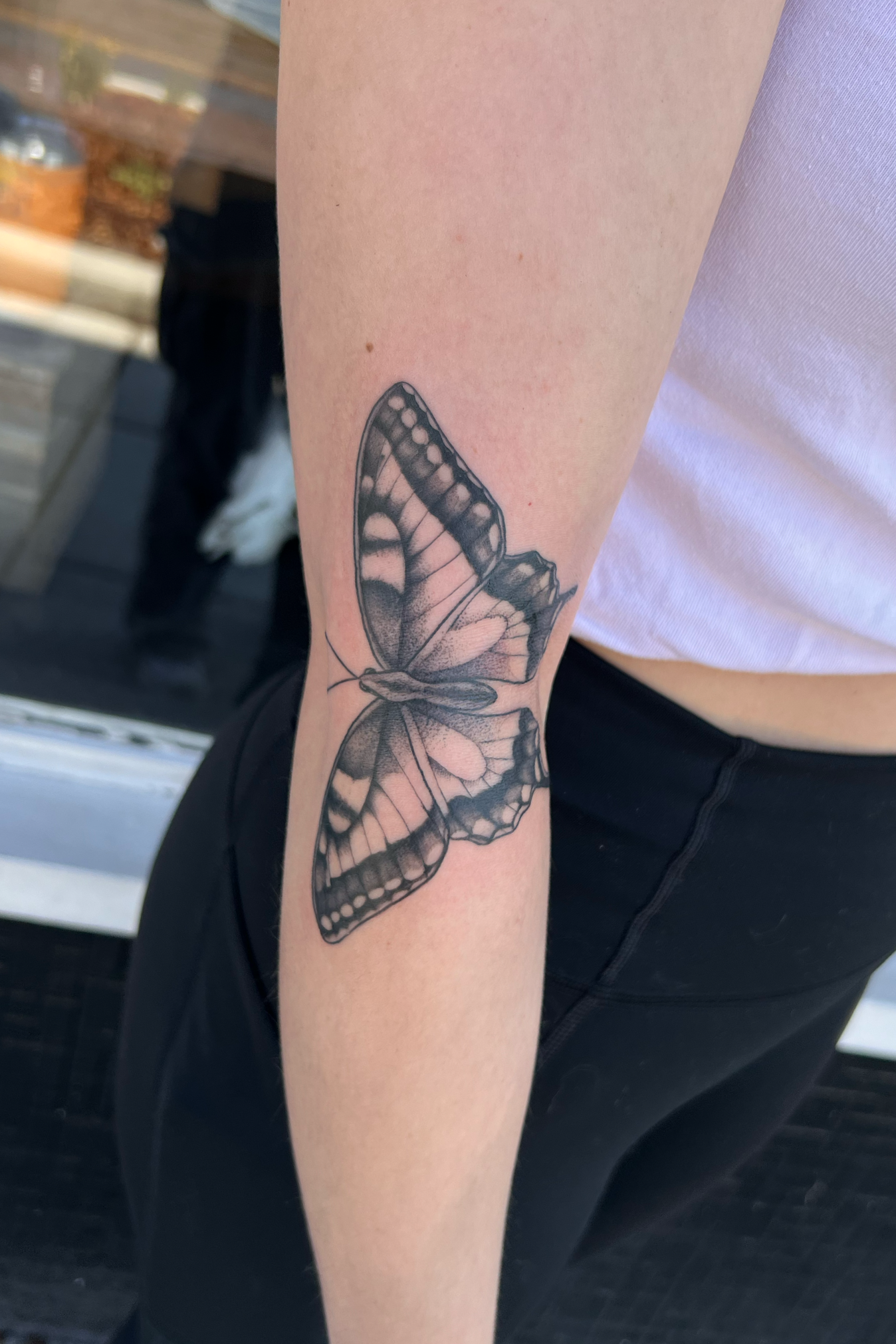 Black and gray tattoo of a butterfly on person's upper arm near the shoulder.