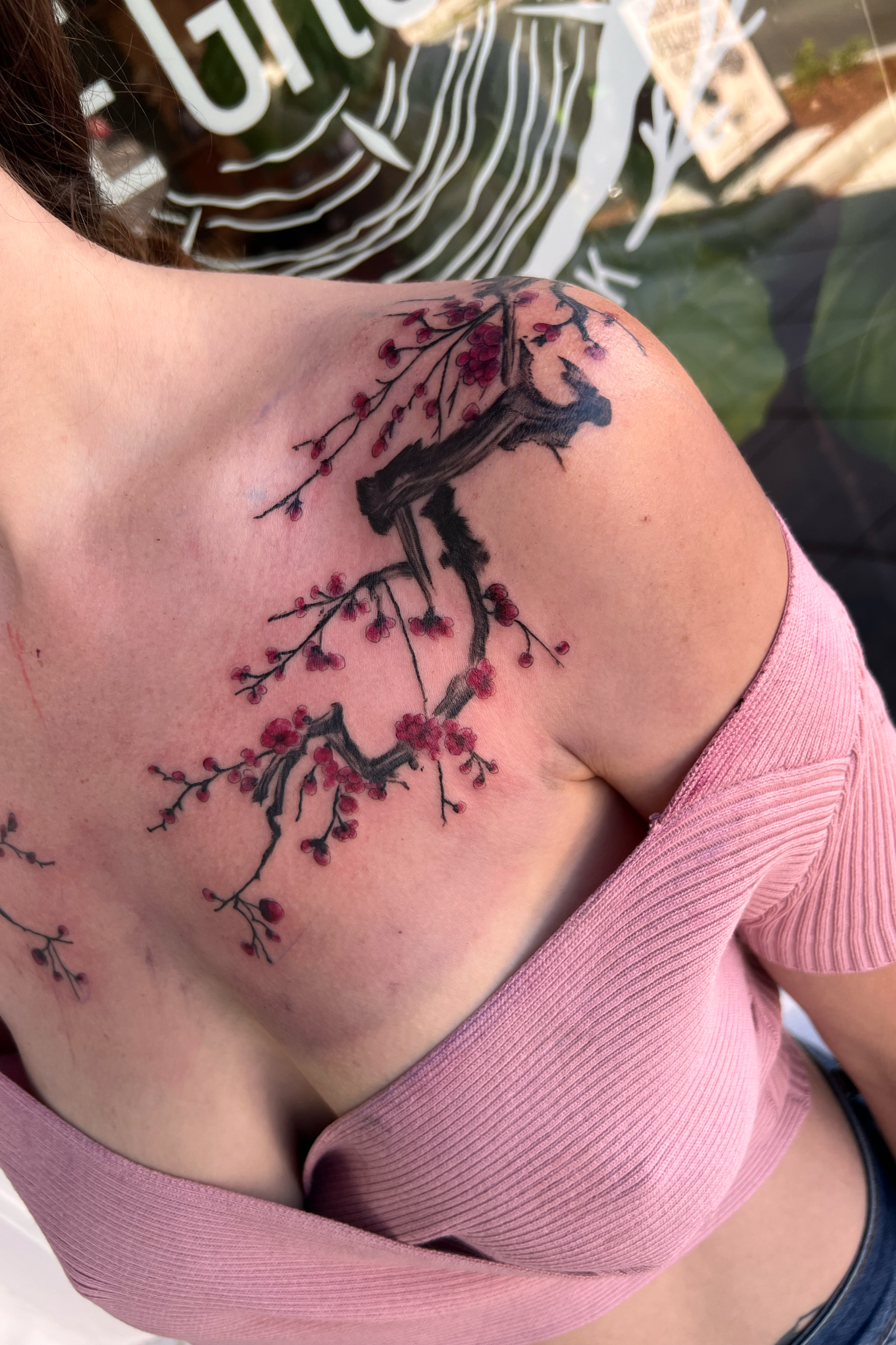 A tattoo of a cherry blossom tree branch with pink flowers on a person's shoulder and upper arm.