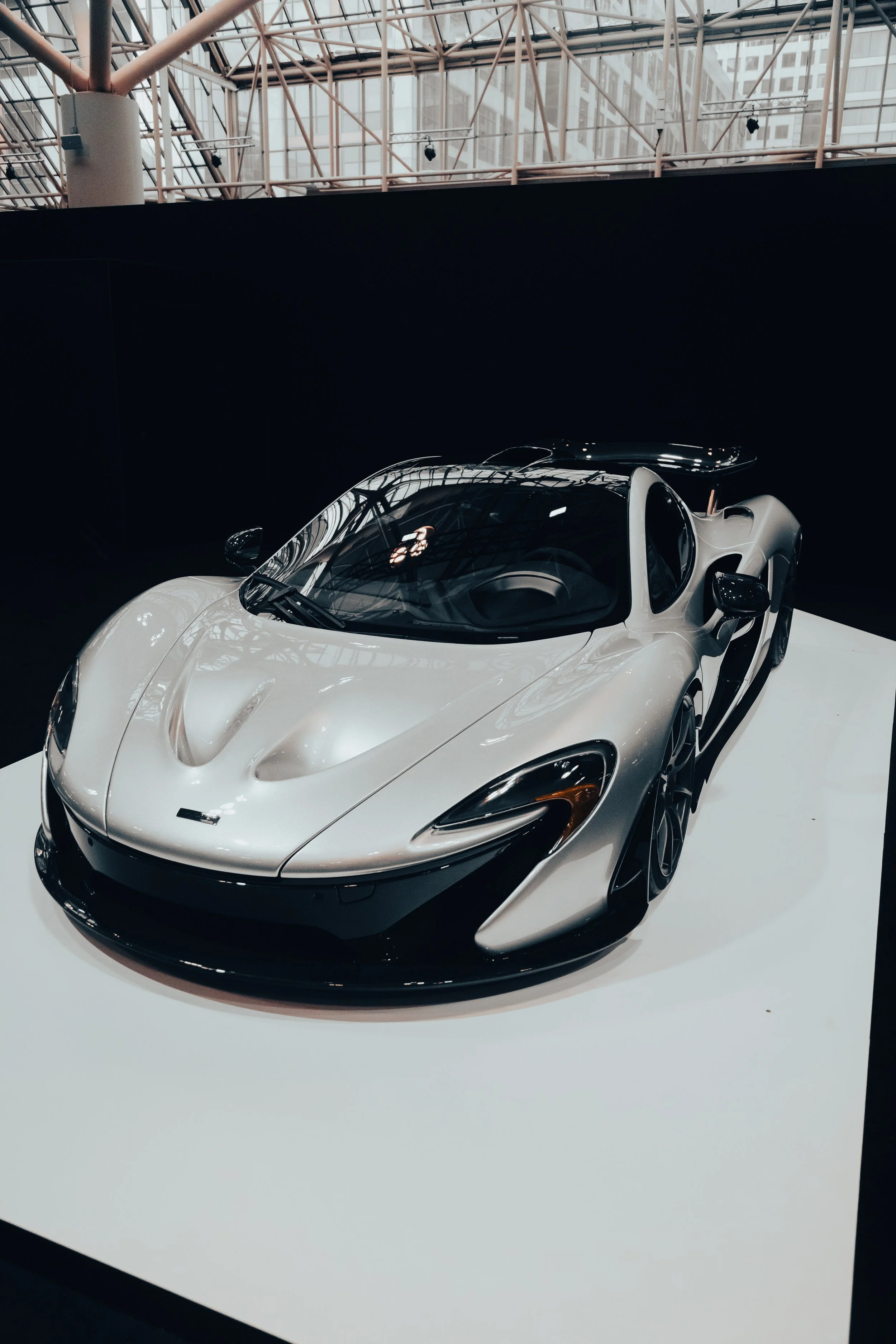 A white sports car on display at an indoor exhibit with reflective glass ceiling.