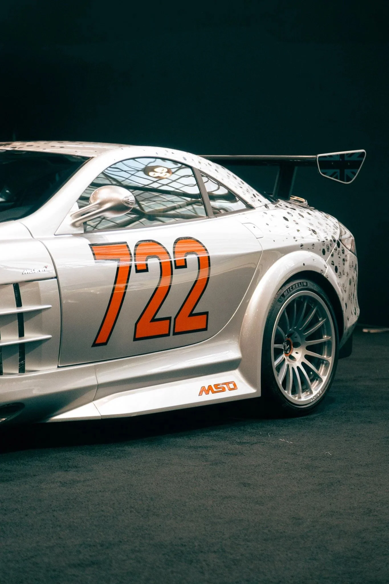 Silver race car with the number 722 in orange on the side, displayed indoors with a black background.