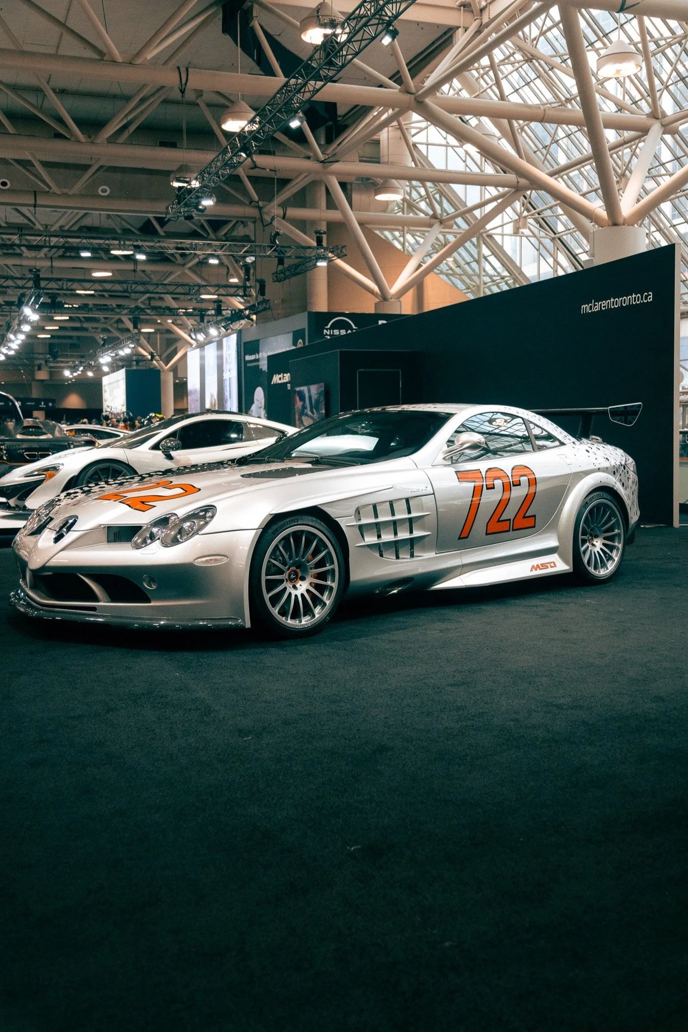 A silver vintage race car with the number 722 painted in orange on the hood and sides, displayed at an indoor car show.